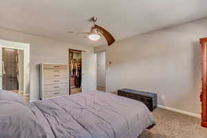 Carpeted bedroom with a spacious closet, connected bathroom, ceiling fan, and a closet