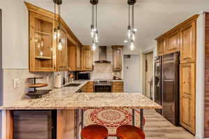 Kitchen with wall chimney range hood, stainless steel appliances, sink, and kitchen peninsula