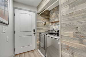 Clothes washing area featuring washer and dryer, light wood-type flooring, and wood walls