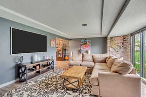 Living room with light hardwood / wood-style flooring, a raised ceiling, and a textured ceiling