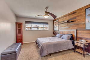 Carpeted bedroom with ceiling fan, a textured ceiling, and wooden walls