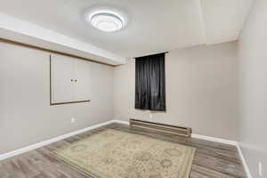 Basement with a textured ceiling, a baseboard radiator, and wood-type flooring