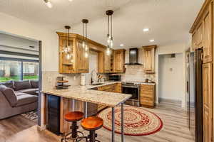 Kitchen featuring wall chimney range hood, sink, hanging light fixtures, stainless steel appliances, and kitchen peninsula