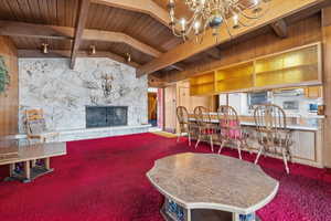 Dining room featuring a stone fireplace, an inviting chandelier, wooden ceiling, beam ceiling, and carpet