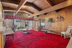 Interior space with lofted ceiling with beams, carpet floors, a chandelier, and wood walls