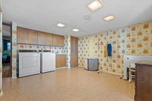 Clothes washing area with cabinets, washing machine and dryer, and a textured ceiling