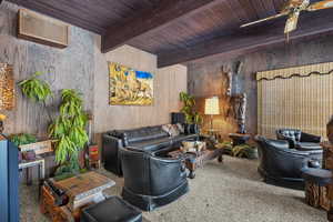 Carpeted living room with ceiling fan, wooden ceiling, beam ceiling, and wood walls