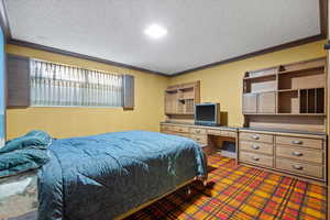 Carpeted bedroom with ornamental molding, built in desk, and a textured ceiling