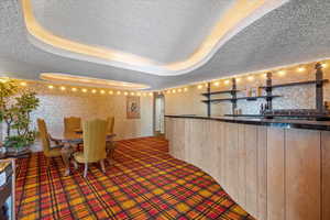 Unfurnished dining area with wooden walls, carpet floors, a tray ceiling, bar area, and a textured ceiling