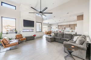 Living room featuring ceiling fan, a high ceiling, and light wood-type flooring