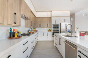 Kitchen with sink, appliances with stainless steel finishes, light hardwood / wood-style floors, custom range hood, and white cabinets