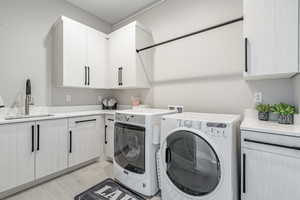 Washroom with sink, cabinets, washing machine and clothes dryer, and light wood-type flooring