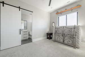 Carpeted bedroom featuring connected bathroom and a barn door