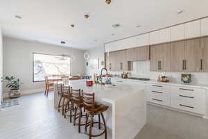 Kitchen with sink, hanging light fixtures, light stone counters, stainless steel gas cooktop, and a center island with sink