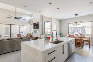 Kitchen with sink, white cabinetry, hanging light fixtures, light hardwood / wood-style floors, and a center island with sink