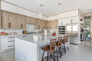 Kitchen with a large island, sink, pendant lighting, stainless steel appliances, and light stone counters