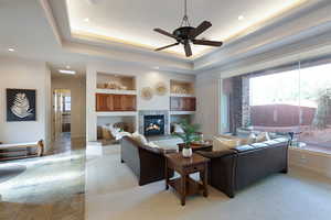 Living room with a premium fireplace, a healthy amount of sunlight, ceiling fan, and a tray ceiling