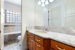 Bathroom featuring vanity, tiled bath, and toilet