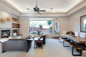 Living room with a tiled fireplace, light colored carpet, a raised ceiling, and ceiling fan