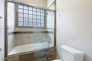 Bathroom with toilet and combined bath / shower with glass door