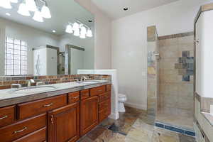 Bathroom with vanity, backsplash, toilet, and a tile shower