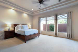 Bedroom with a raised ceiling, light colored carpet, and ceiling fan