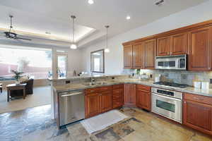 Kitchen with decorative light fixtures, sink, kitchen peninsula, stainless steel appliances, and light stone countertops