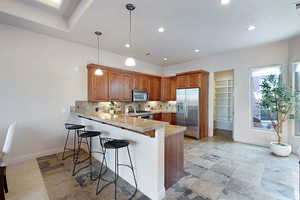 Kitchen featuring a breakfast bar, tasteful backsplash, hanging light fixtures, appliances with stainless steel finishes, and kitchen peninsula