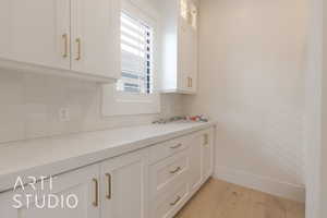 Kitchen featuring white cabinetry, sink, decorative backsplash, light hardwood / wood-style floors, and light stone counters