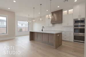 Kitchen with white cabinetry, premium range hood, hanging light fixtures, and a kitchen island with sink