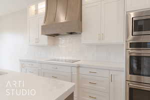 Kitchen with premium range hood, appliances with stainless steel finishes, white cabinets, light stone countertops, and backsplash