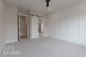 primary bedroom featuring ceiling fan, a barn door, and light carpet