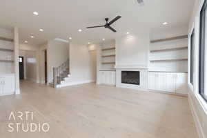 Unfurnished living room featuring light hardwood / wood-style flooring, built in features, a large fireplace, and ceiling fan