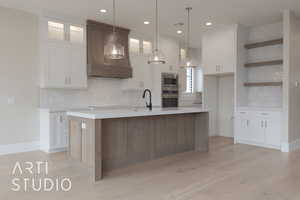 Kitchen with white cabinetry, decorative light fixtures, stainless steel appliances, and a center island with sink