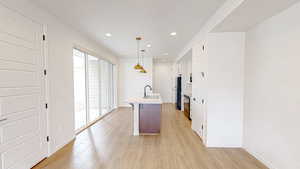 Kitchen featuring sink, refrigerator, a kitchen island with sink, hanging light fixtures, and light wood-type flooring