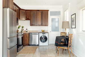 Kitchen with washer / dryer, light stone countertops, appliances with stainless steel finishes, and light tile patterned floors