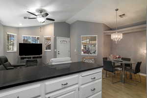 Kitchen with ceiling fan with notable chandelier, decorative light fixtures, white cabinetry, lofted ceiling, and light wood-type flooring