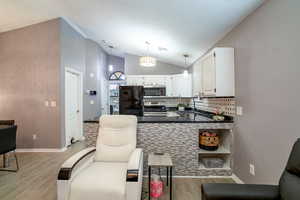 Kitchen featuring white cabinetry, tasteful backsplash, vaulted ceiling, light wood-type flooring, and appliances with stainless steel finishes