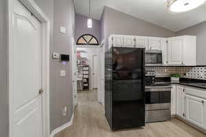 Kitchen with white cabinetry, light hardwood / wood-style flooring, lofted ceiling, and appliances with stainless steel finishes