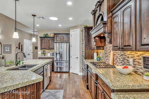 Kitchen with stainless steel appliances, sink, dark brown cabinetry, and light stone counters