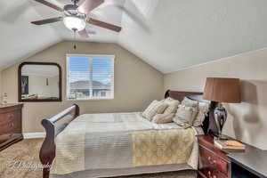 Bedroom with ceiling fan, lofted ceiling, carpet flooring, and a textured ceiling