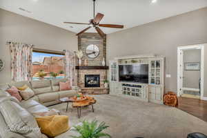 Carpeted living room with ceiling fan, a large fireplace, and high vaulted ceiling