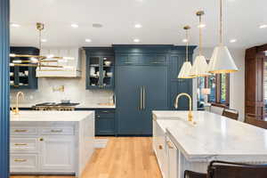 Kitchen featuring an island with sink, light stone countertops, pendant lighting, and paneled built in fridge