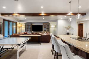 Kitchen with hanging light fixtures, beam ceiling, light colored carpet, light stone counters, and black electric cooktop