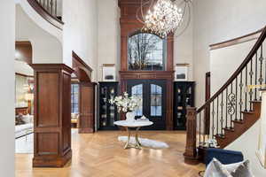 Foyer with a high ceiling, light parquet flooring, and a notable chandelier