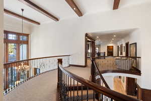 Hall with beam ceiling, carpet floors, and a chandelier