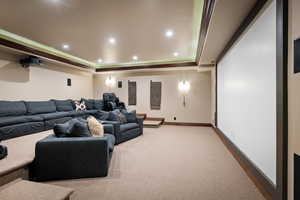 Cinema room featuring a raised ceiling, crown molding, and carpet floors