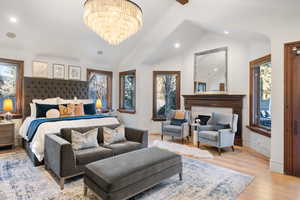 Bedroom featuring a chandelier, a high end fireplace, light hardwood / wood-style floors, and vaulted ceiling