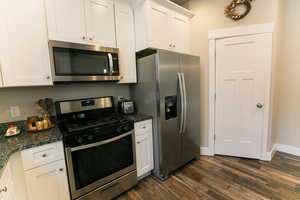 Kitchen with white cabinetry, appliances with stainless steel finishes, dark wood-type flooring, and dark stone counters