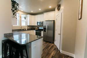 Kitchen featuring white cabinetry, dark stone countertops, stainless steel appliances, a kitchen bar, and kitchen peninsula